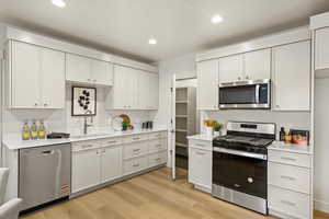 Kitchen featuring stainless steel appliances, white cabinetry, light wood finished floors, recessed lighting, and light stone counters