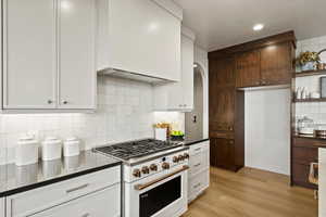 Two tone kitchen featuring high end range, arched walkways, backsplash, open shelves, and light wood-style floors