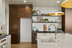 Kitchen with dark stone countertops, arched walkways, high end white range, light wood-style flooring, and decorative light fixtures
