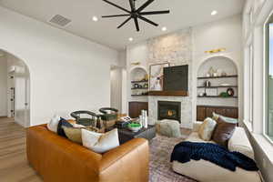 Living room with arched walkways, wood finished floors, built in features, ceiling fan, and a fireplace