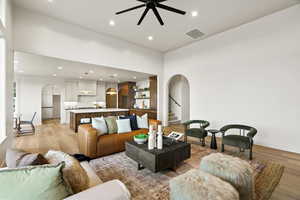 Living room with arched walkways, light wood-type flooring, recessed lighting, and a ceiling fan