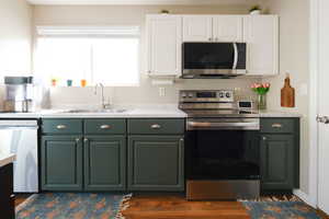 Dual tone kitchen featuring stainless steel appliances, dual tone cabinets, light countertops, and dark wood-style floors