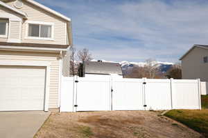 View of side of property featuring a gate, a mountain view, a shingled roof, and driveway