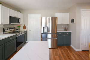 Kitchen with two tone color scheme, stainless steel appliances, light stone counters, and dark wood-style floors
