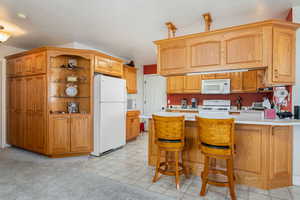 Kitchen with a peninsula, light countertops, white appliances, a kitchen bar, and light colored carpet