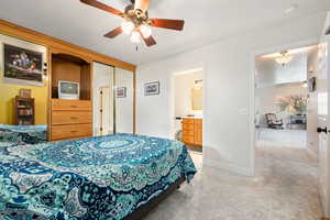 Bedroom featuring light colored carpet, a closet, a ceiling fan, and ensuite bath