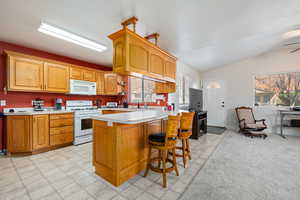 Kitchen featuring light countertops, white appliances, lofted ceiling, a breakfast bar, and wood finish cabinetry
