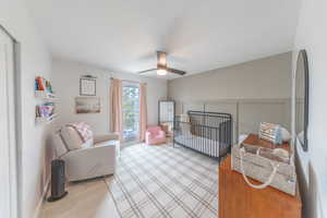 Bedroom with a crib, a decorative wall, a ceiling fan, and light wood-style floors