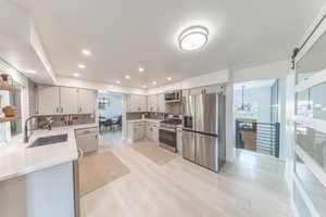 Kitchen with stainless steel appliances, tasteful backsplash, light wood finished floors, recessed lighting, light quartz countertops, modern barn door with large hidden pantry