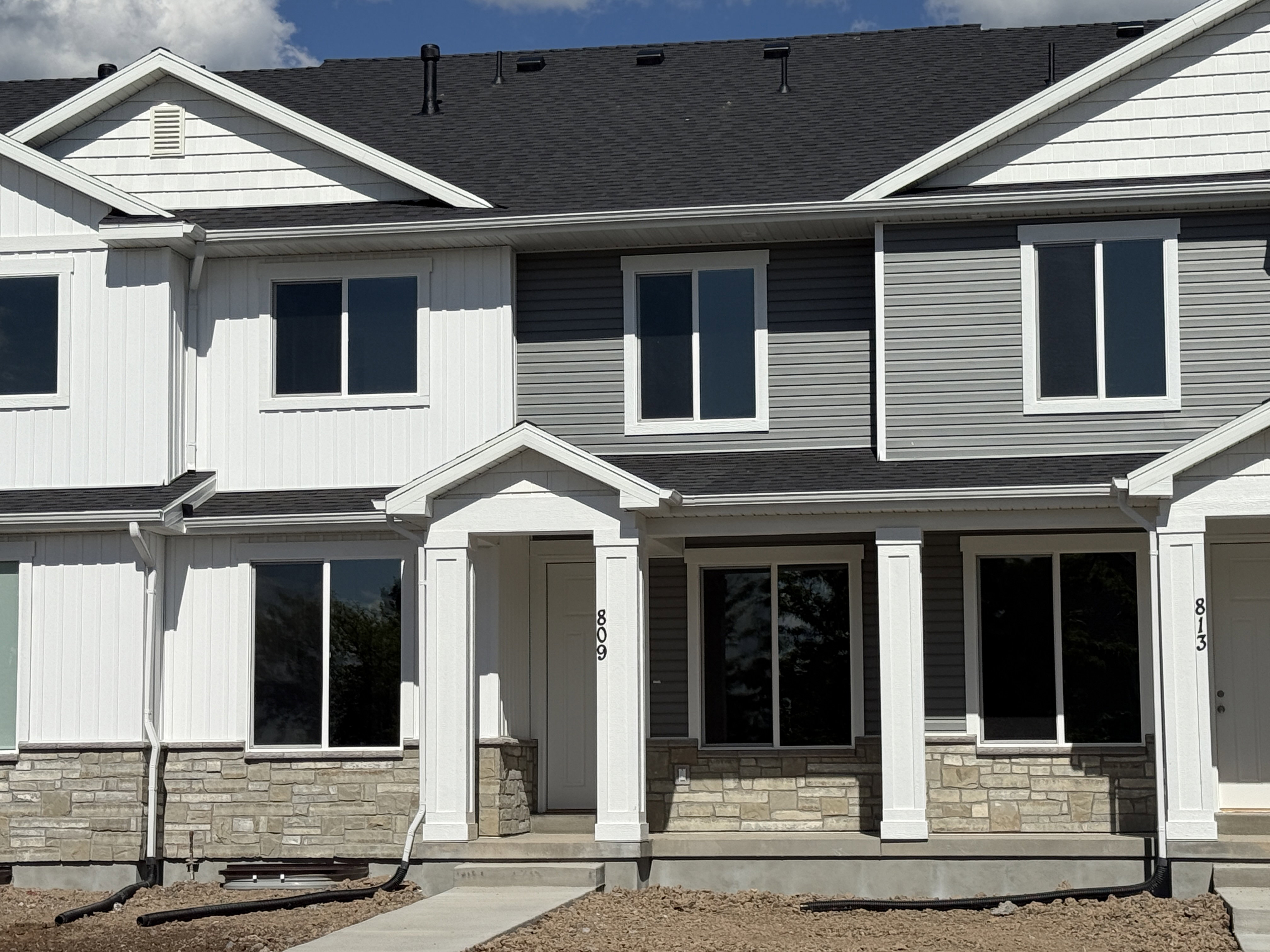 Contemporary townhome exterior featuring a stone accent foundation, horizontal and vertical siding, a covered entry porch with columns, and a dark shingle roof