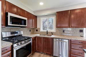 Kitchen with stainless steel appliances, light stone counters, and backsplash