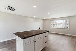 Kitchen featuring butcher block counters, white cabinetry, a kitchen island, dark wood-style floors, and recessed lighting