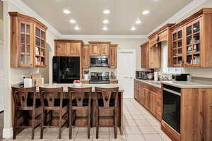 Kitchen featuring glass fronted cabinets, a breakfast bar, light countertops, black appliances, and a peninsula