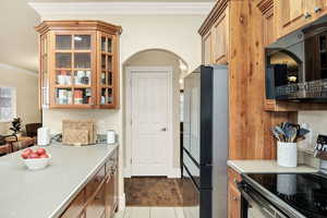 Kitchen with crown molding, electric stove, freestanding refrigerator, light countertops, and wood finish cabinets