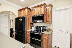 Kitchen with stainless steel appliances, light countertops, wood finish cabinets, ornamental molding, and arched walkways