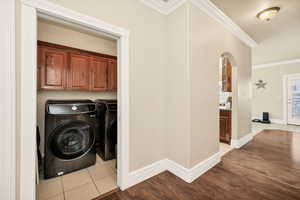 Laundry area featuring crown molding, arched walkways, light wood-style flooring, washer and dryer, and cabinet space