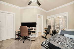 Bedroom featuring light colored carpet, an office area, ornamental molding, a closet, and a ceiling fan