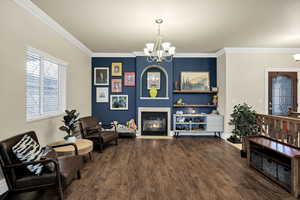Sitting room with a chandelier, a tiled fireplace, dark wood finished floors, and crown molding