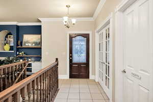 Foyer featuring ornamental molding, light tile patterned floors, and suspended lighting