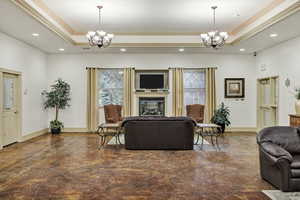Living room featuring suspended lighting, a tray ceiling, healthy amount of natural light, a glass covered fireplace, and ornamental molding