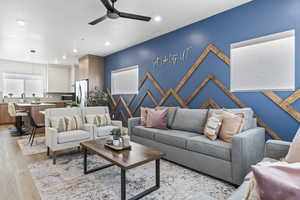 Living room featuring an accent wall, ceiling fan, light wood-style flooring, and recessed lighting