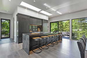 Kitchen with a skylight, modern cabinets, a spacious island, a kitchen breakfast bar, and dark stone counters