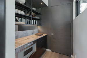 Kitchen featuring light stone countertops, light wood-style flooring, dark cabinetry, stainless steel microwave, and open shelves