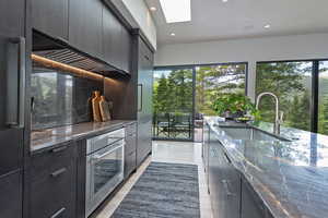 Kitchen with modern cabinets, dark cabinetry, a skylight, oven, and recessed lighting