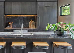 Kitchen with dark stone counters, a kitchen bar, backsplash, and modern cabinets