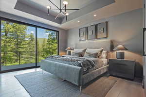 Bedroom featuring a raised ceiling, access to exterior, a chandelier, and light wood-type flooring