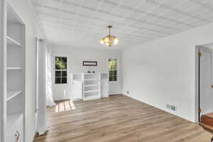 Unfurnished living area with suspended lighting, light wood finished floors, healthy amount of natural light, an ornate ceiling