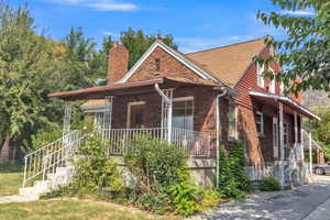 View of front of home featuring brick siding, covered porch, a chimney, and a shingled roof