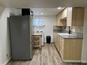 Kitchen with light wood finish cabinets, freestanding refrigerator, light wood-type flooring, white range with electric cooktop, and dark countertops