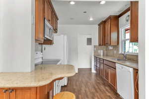 Kitchen featuring wood finish cabinets, white appliances, dark wood-type flooring, light stone counters, and recessed lighting