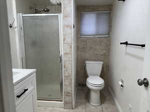 Bathroom with vanity, a stall shower, light tile patterned floors, and tile walls