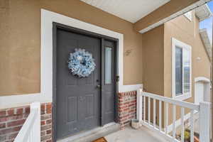 Property entrance featuring brick siding, stucco siding, and covered porch