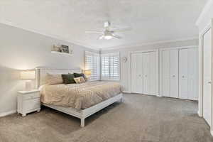 Carpeted bedroom with multiple closets, crown molding, a textured ceiling, and ceiling fan