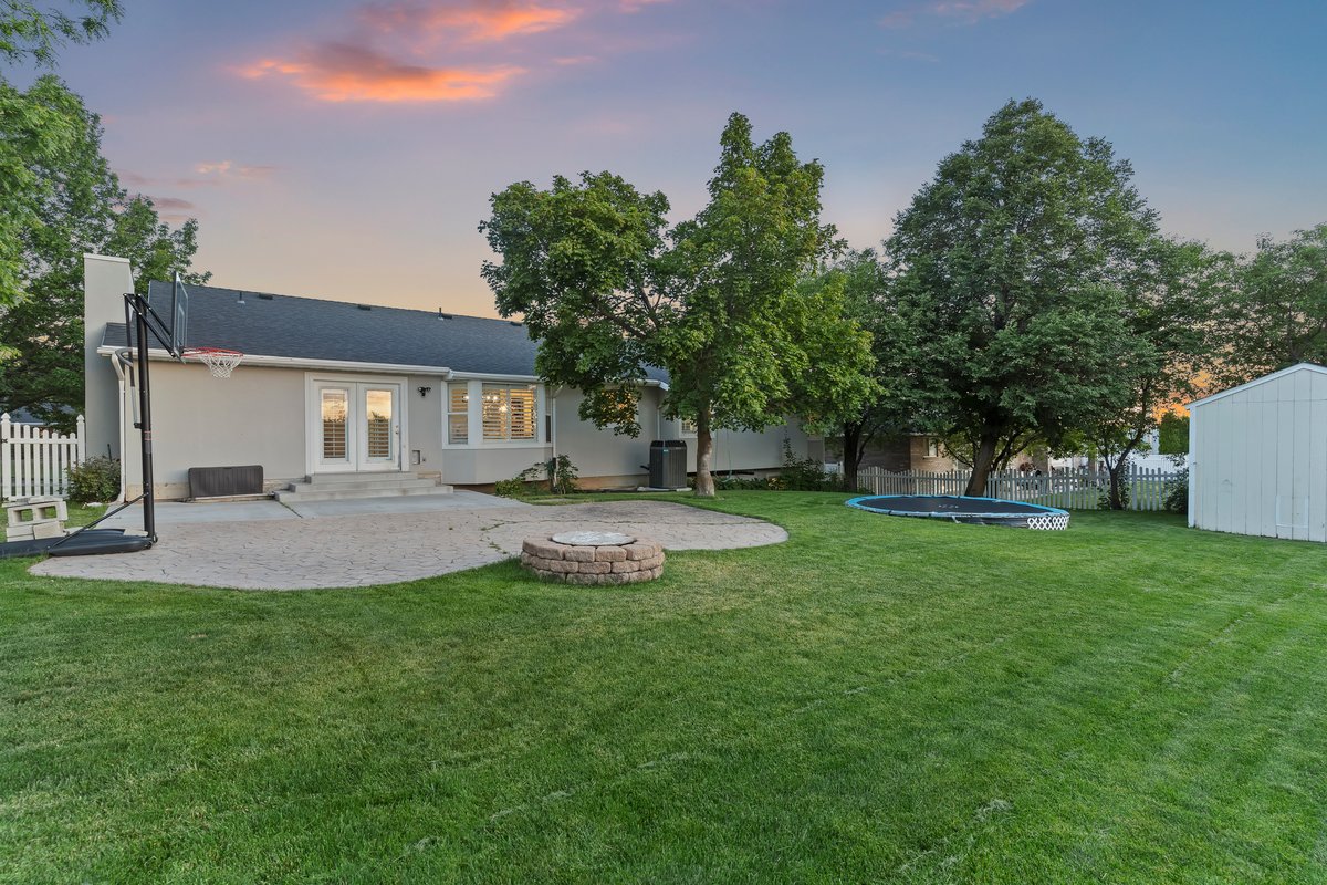 Expansive backyard featuring a manicured lawn, established trees, and a durable white picket fence
