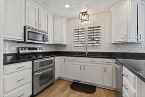 Kitchen featuring stainless steel appliances, white cabinetry, dark stone countertops, light wood-style flooring, and a textured ceiling