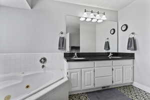 Bathroom featuring double vanity, a whirlpool tub, a textured ceiling, and light tile patterned floors
