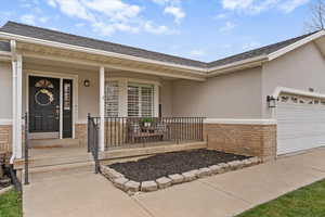 Entrance to property featuring brick siding, stucco siding, a porch, and a garage