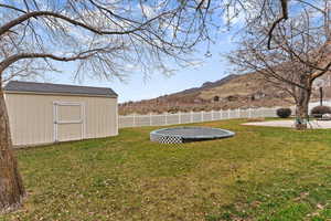 Fenced backyard featuring a shed, a trampoline, and a mountain view