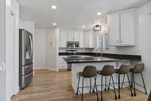 Kitchen with dark stone countertops, white cabinets, stainless steel appliances, light wood-style flooring, and recessed lighting
