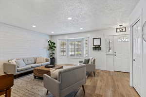Living room featuring an accent wall, light wood-style floors, recessed lighting, a textured ceiling, and wood walls