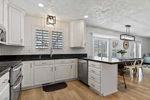Kitchen featuring a kitchen bar, stainless steel appliances, light wood-style floors, suspended lighting, and white cabinetry