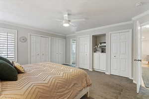 Bedroom with two closets, dark carpet, a textured ceiling, ornamental molding, and a ceiling fan