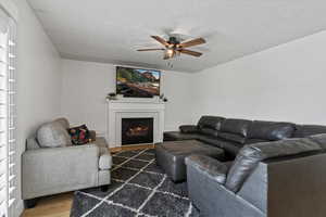 Living area with wood finished floors, a ceiling fan, a tile fireplace, and a textured ceiling