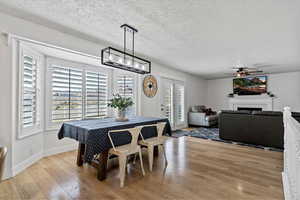 Dining room featuring light wood-style flooring, ceiling fan, a fireplace, and a textured ceiling