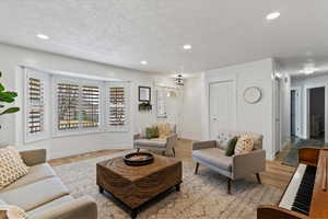 Living area with light wood finished floors, a textured ceiling, and recessed lighting