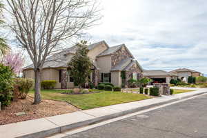 View of front of property featuring stone siding, stucco siding, a front lawn, and an attached garage